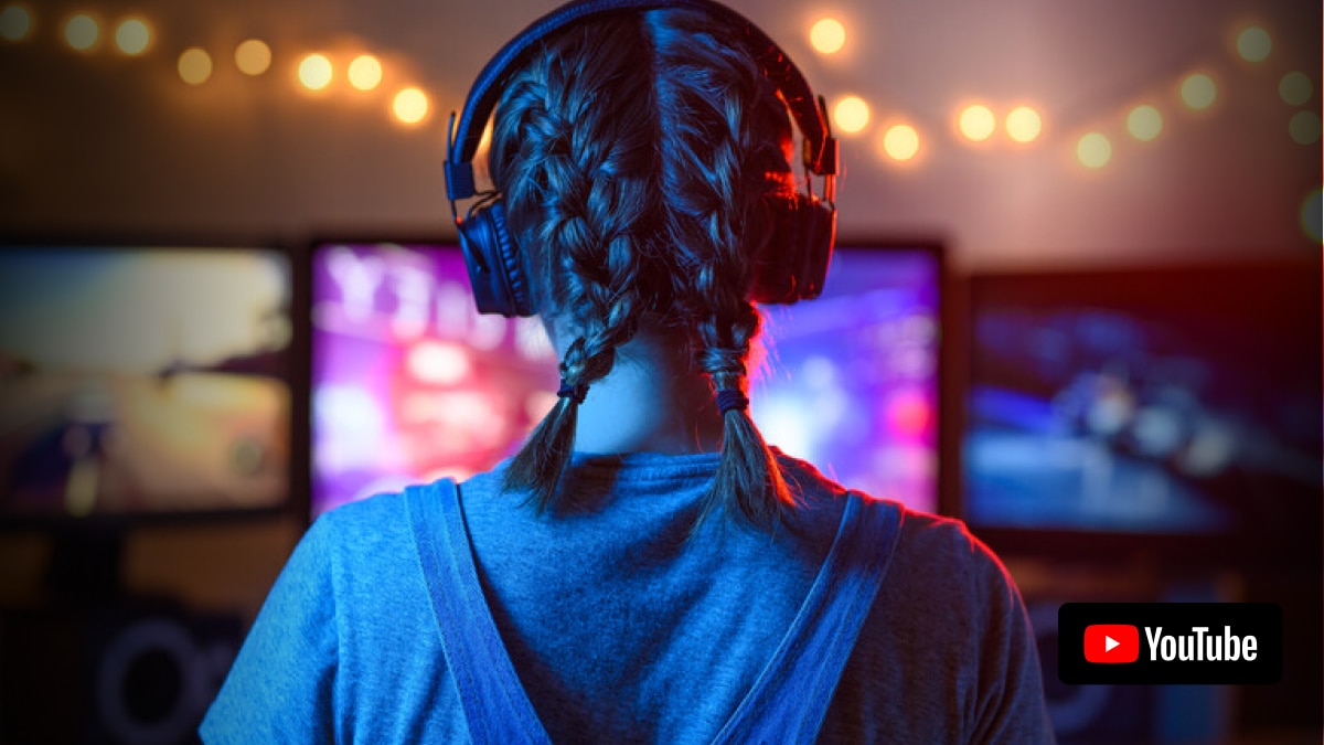 Gamer wearing headphones faces three glowing monitors with blurred neon visuals and string lights.
