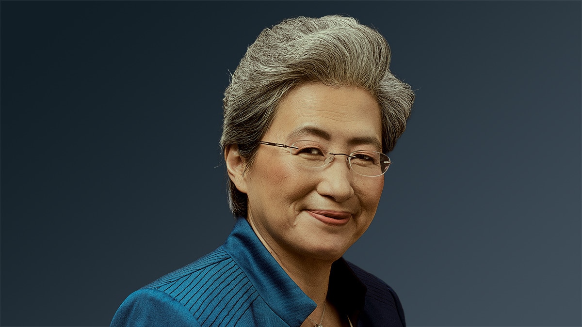 Woman with gray hair and glasses smiling slightly while wearing a blue jacket on a dark background.
