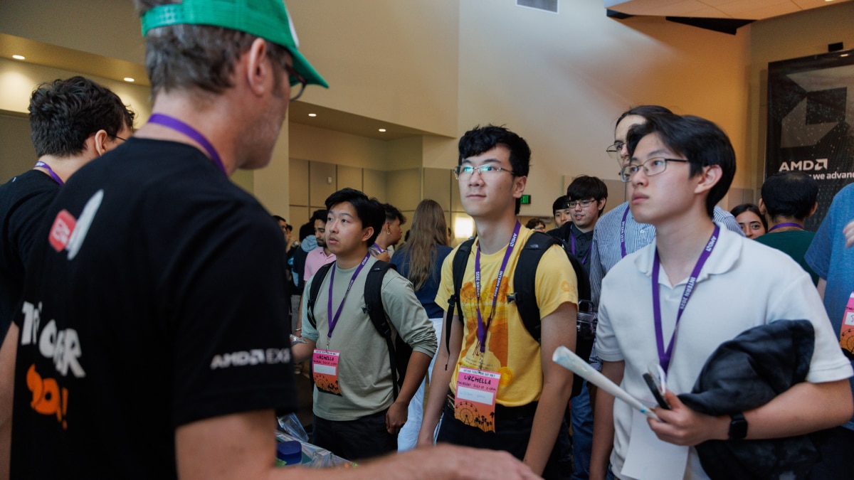 Group of students with event badges listening to AMD staff member at tech event.
