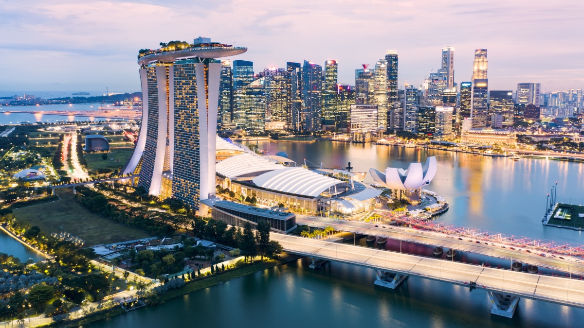 Marina Bay Sands hotel and illuminated Singapore skyline reflected in bay at twilight.