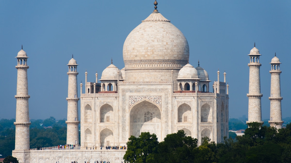 White marble Taj Mahal with central dome and four minarets against clear blue sky.