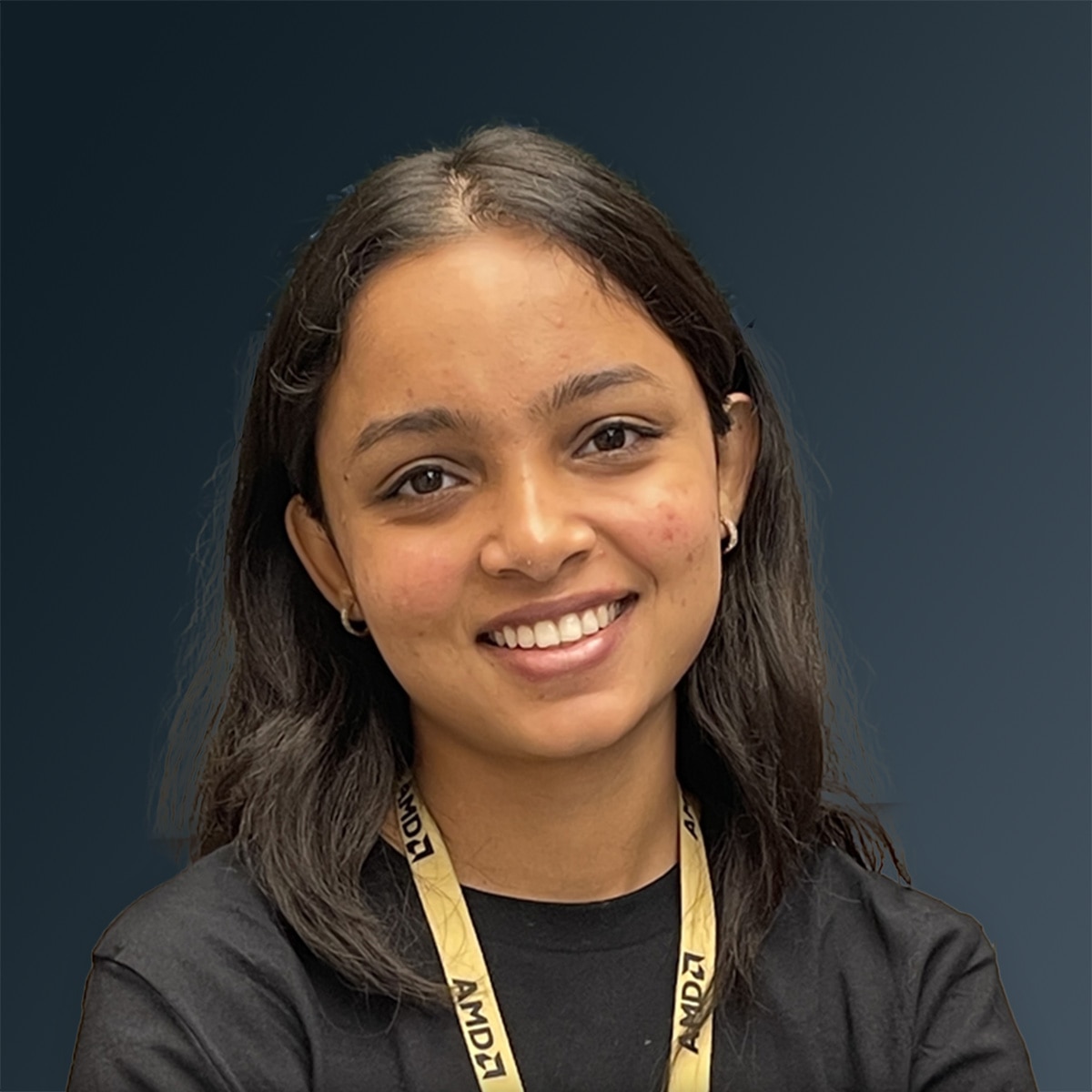 Woman wearing black shirt and AMD lanyard smiling indoors with green plants in background.