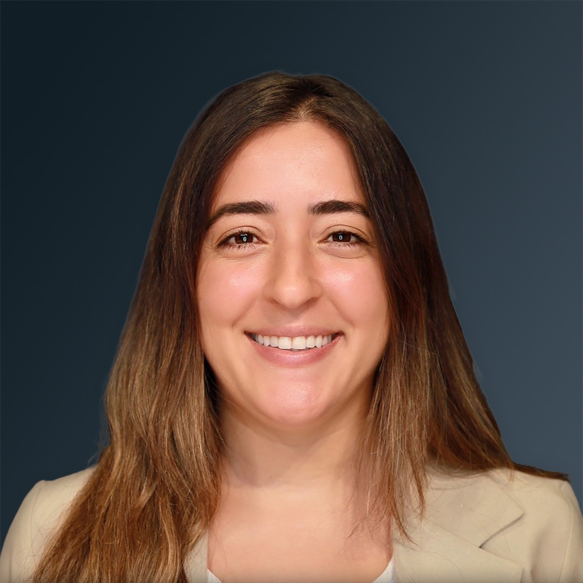 Woman with long brown hair smiling in beige blazer against gray background.