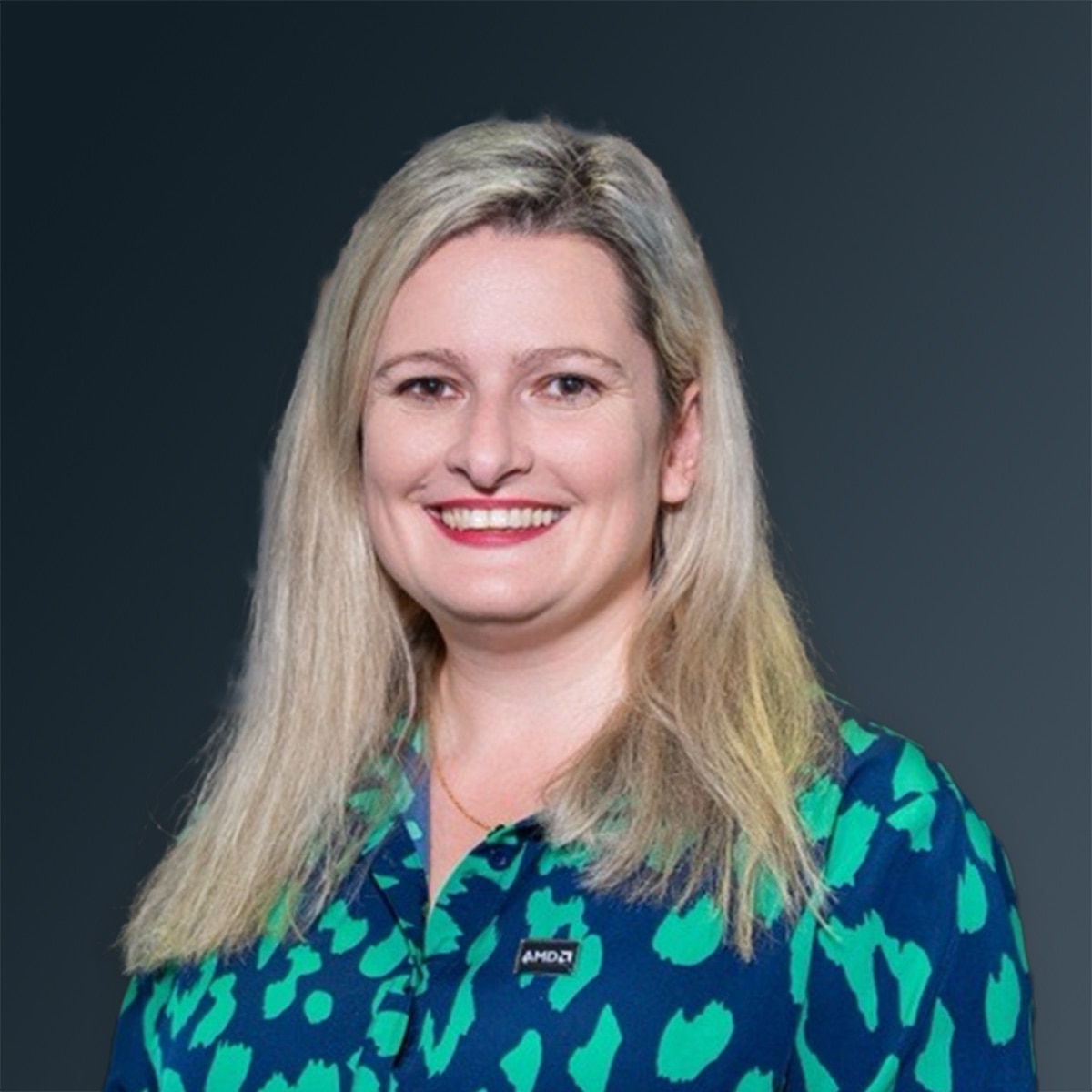 Woman smiling in a blue-green patterned top with blond hair against a dark gradient background.