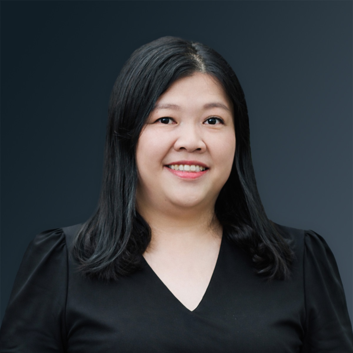 Woman with long black hair wearing a black top, smiling against a dark gradient background.