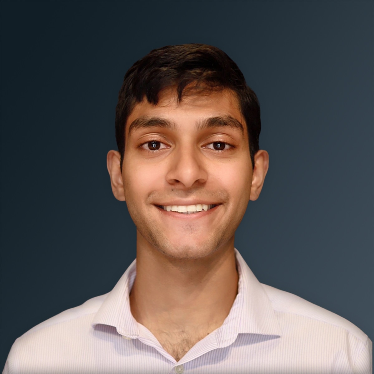 Man in light-colored collared shirt smiling against dark gray background.