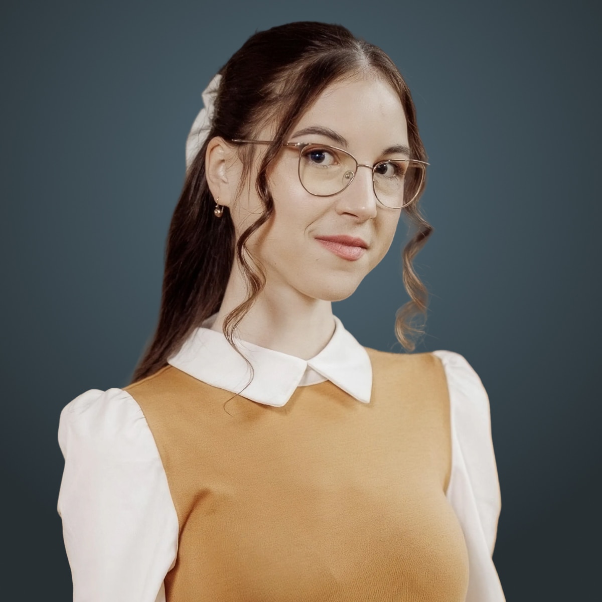 Person with glasses and long brown hair wearing a tan top with white sleeves against a dark teal background.