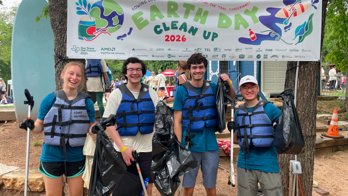 Four volunteers in life vests hold trash bags beneath an Earth Day Clean Up 2026 banner at an outdoor cleanup event.
