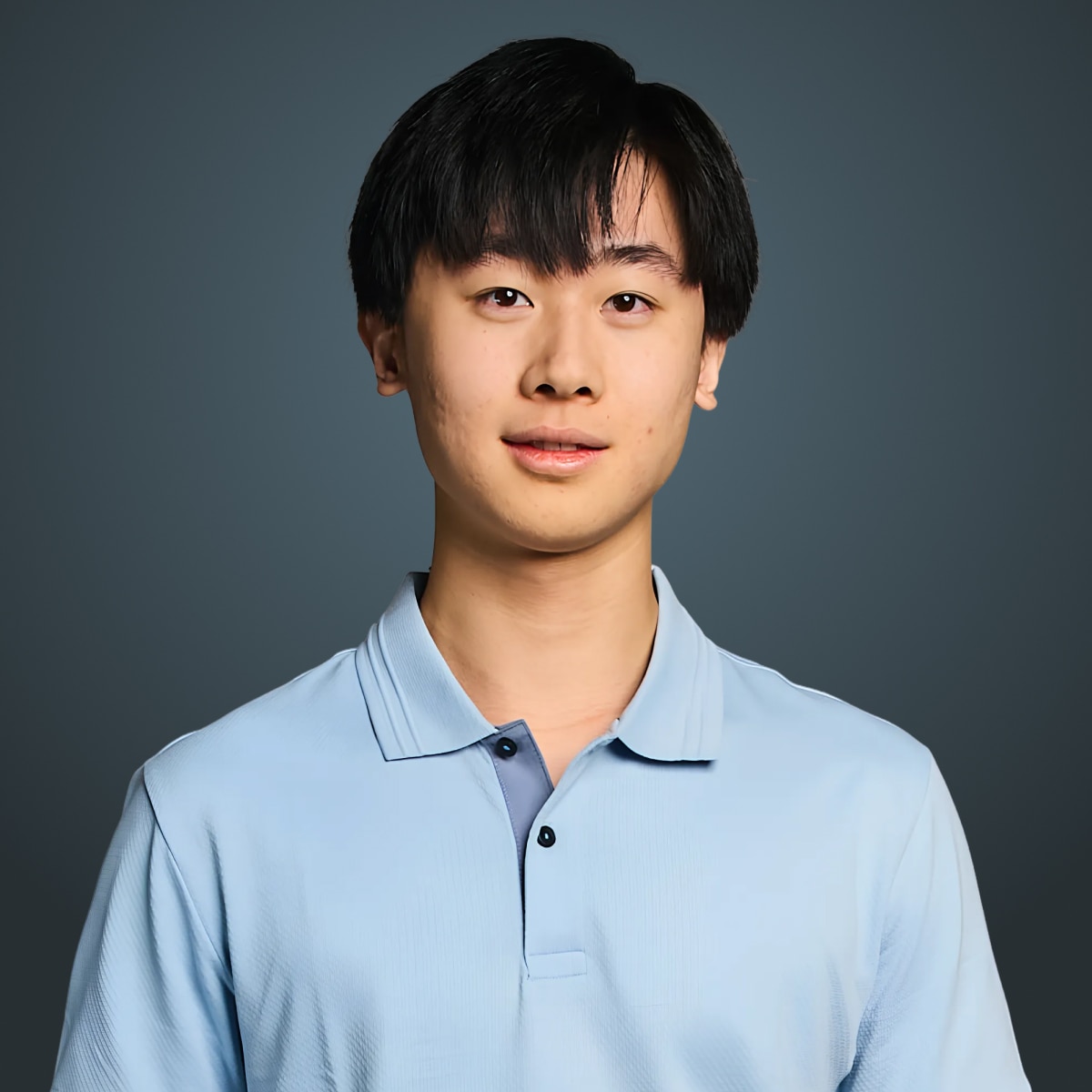 Person with short black hair wearing a light blue polo shirt against a dark teal background