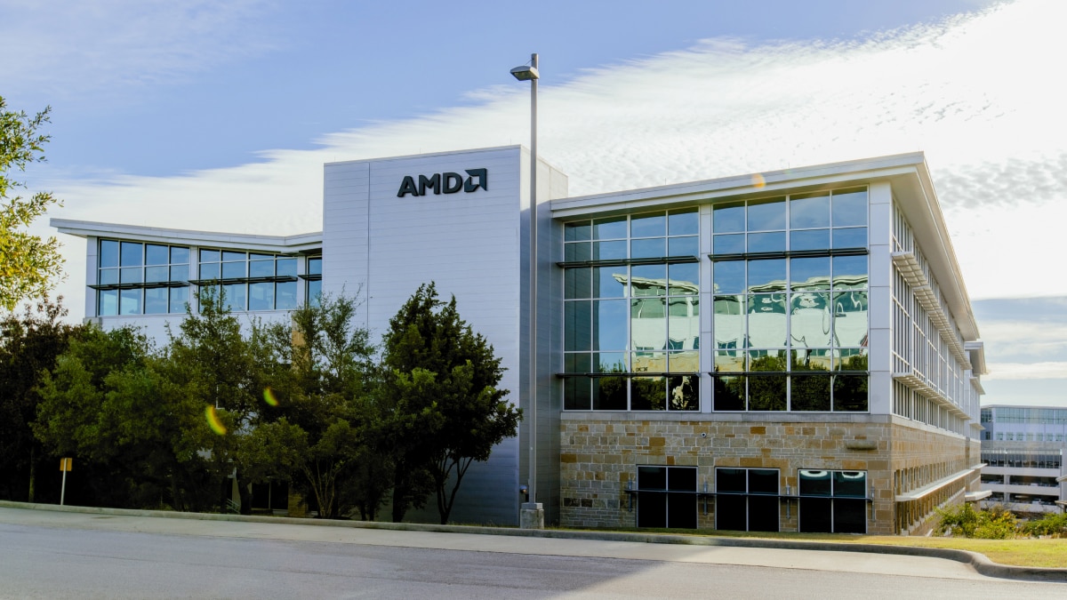 Modern AMD office building with a glass façade, white exterior, and landscaped trees under a blue sky.