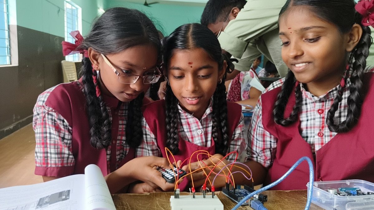 Three students in school uniforms assemble and test an electronics project with wires and a keypad in a classroom.