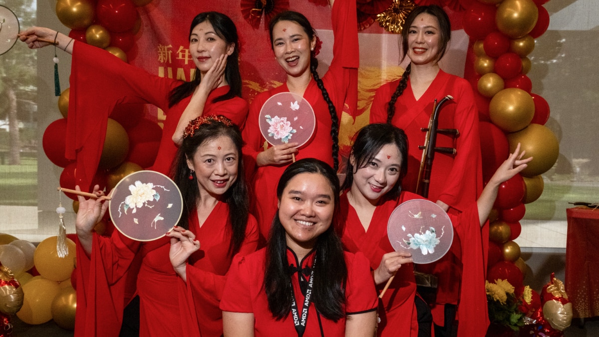 Group wearing colorful traditional Japanese attire poses in front of an AMD event backdrop decorated with hanging paper cranes.