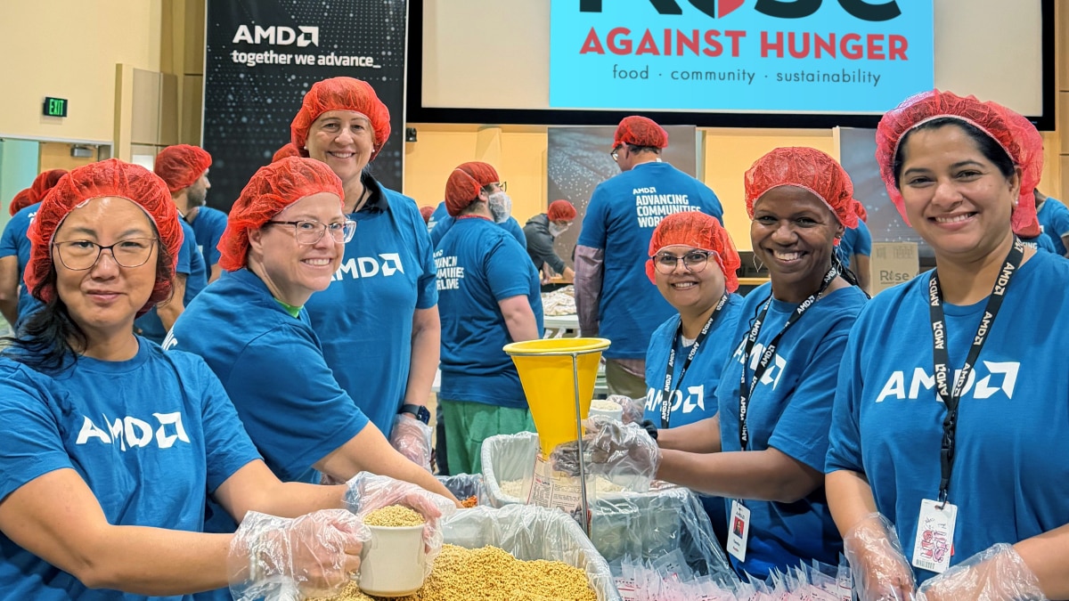 AMD volunteers wearing blue shirts, gloves, and red hairnets package meals at a Rise Against Hunger event. Screen reads "Rise Against Hunger."