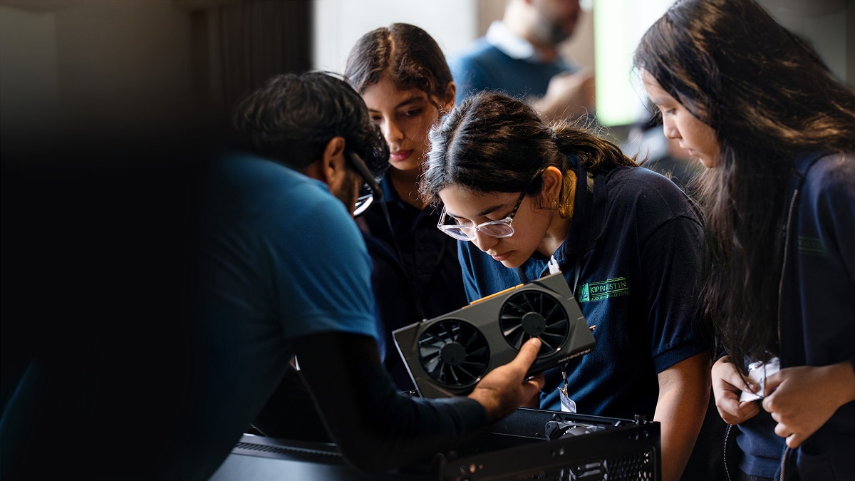 Students work together with a mentor to assemble a desktop computer, examining a graphics card during a hands-on STEM workshop.