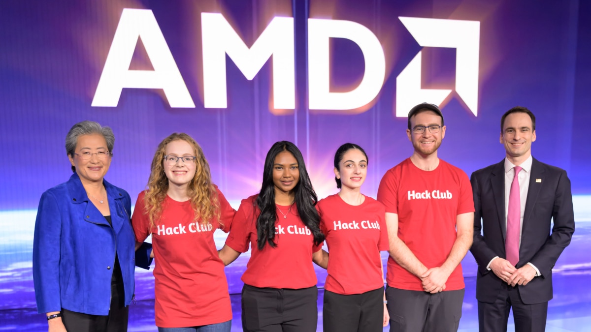 Group photo of Hack Club participants in red shirts with guests in front of a large AMD backdrop at a technology event.
