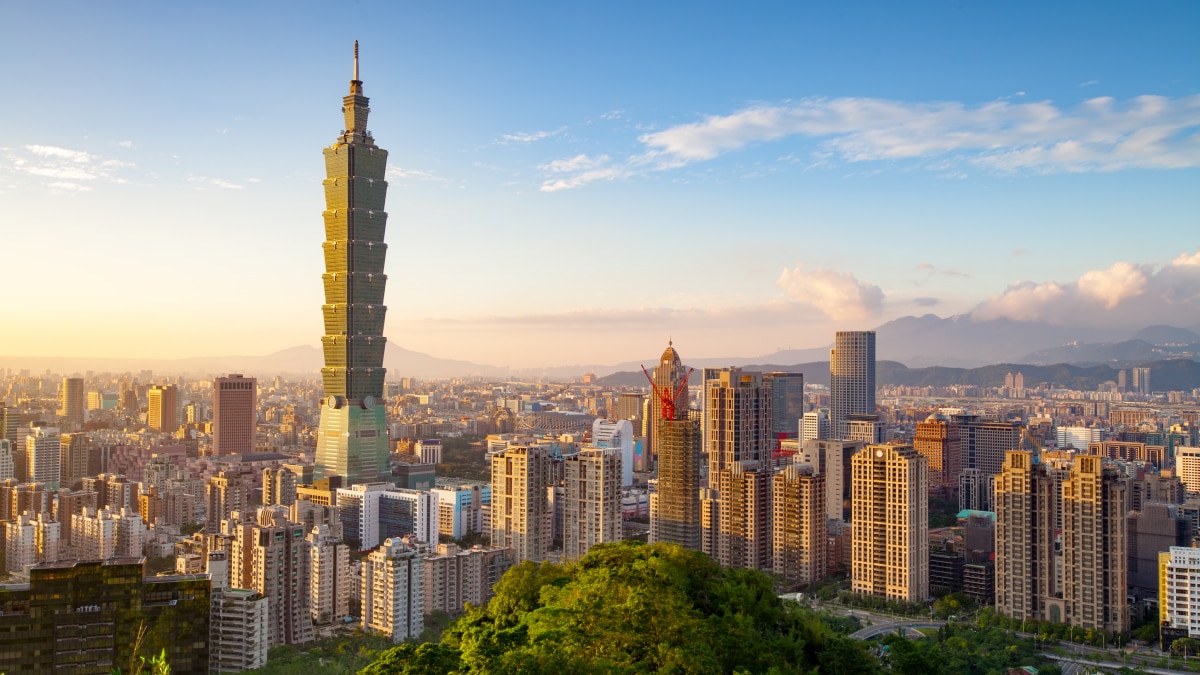 Taipei skyline at sunset with the iconic Taipei 101 skyscraper surrounded by modern high-rise buildings and mountains in the background.