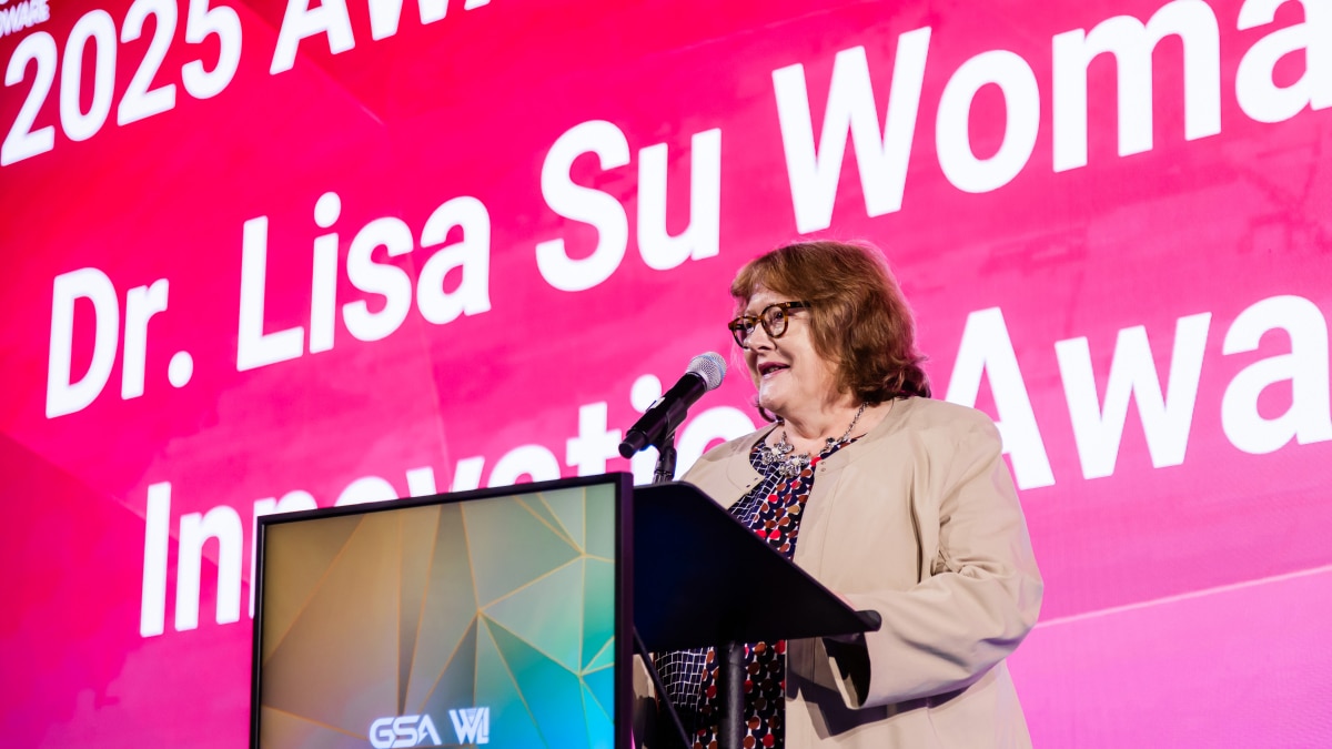 a presenter speaking at a podium during an innovation award event with large pink presentation screen backdrop