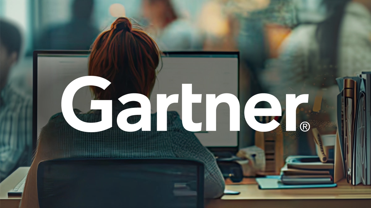 Person working at desktop computer with large “Gartner®” text overlay, office desk with books and supplies visible