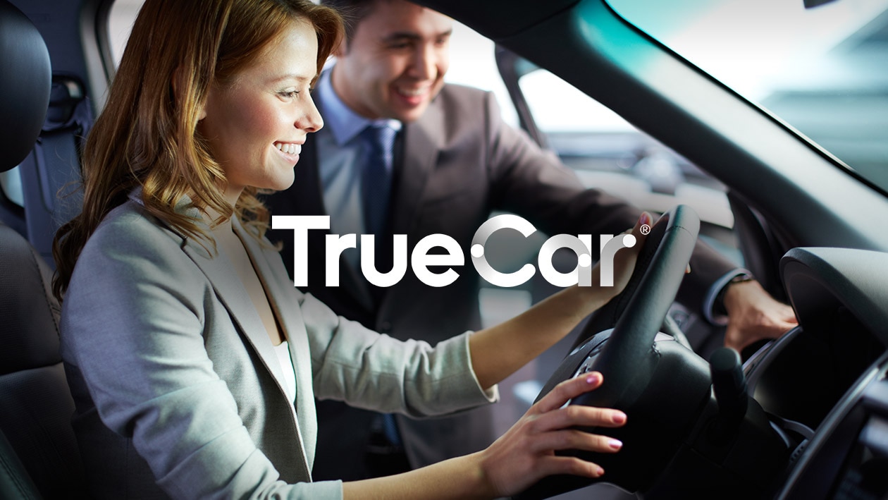 Automotive: TrueCar and AWS Image showing TrueCar logo in white color with woman inside a car driving