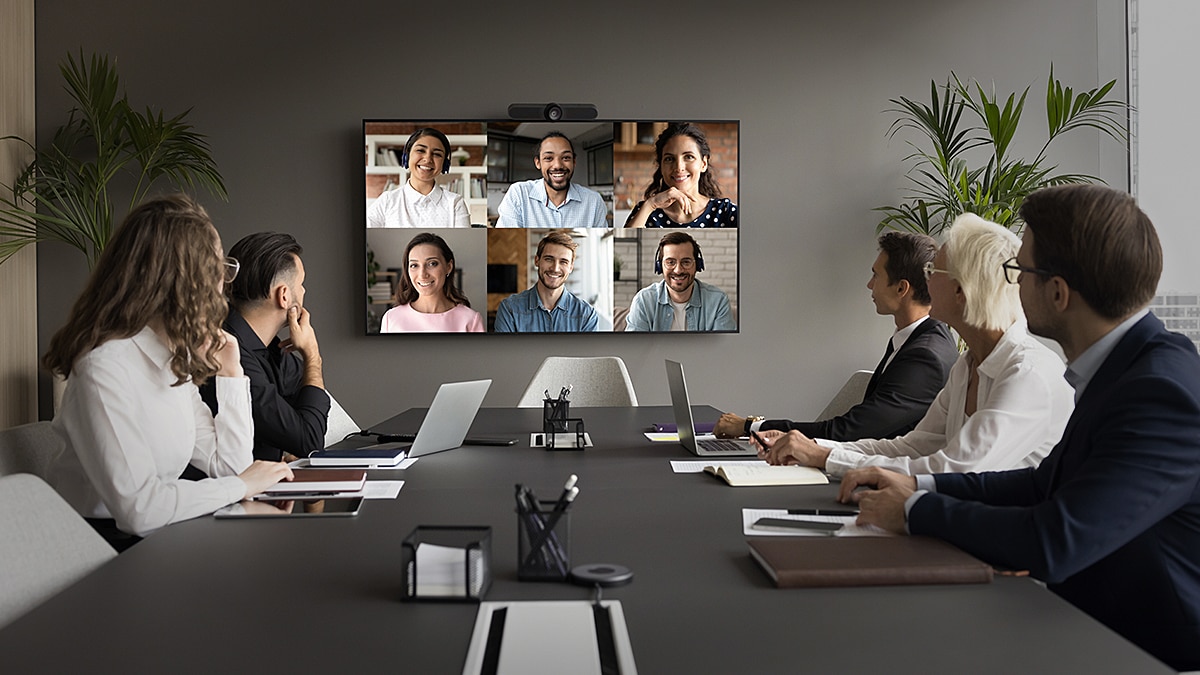 Business team sitting in a conference room having a hybrid meeting with colleagues displayed on a large screen for a video call.