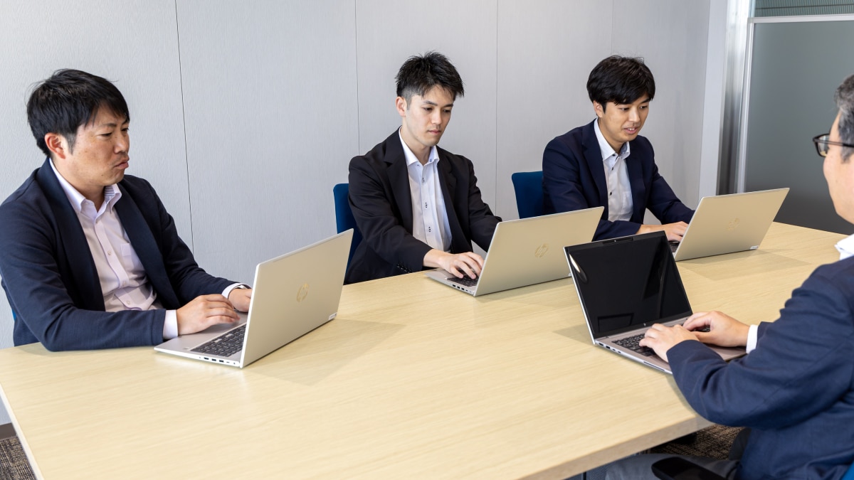 Four people seated at a conference table working on HP laptops during a meeting.