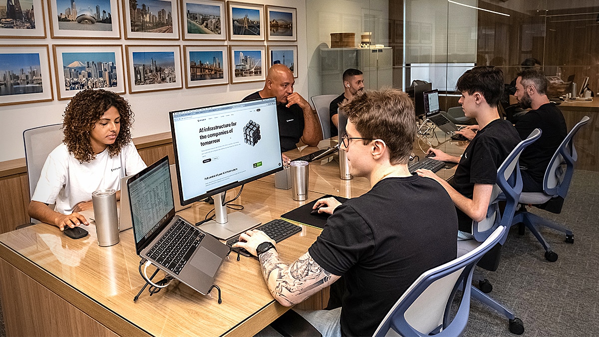Group of people working at laptops in a glass-walled office, screen showing AI infrastructure website.