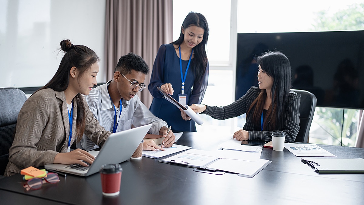 Four colleagues in a meeting reviewing documents and laptops around a conference table.