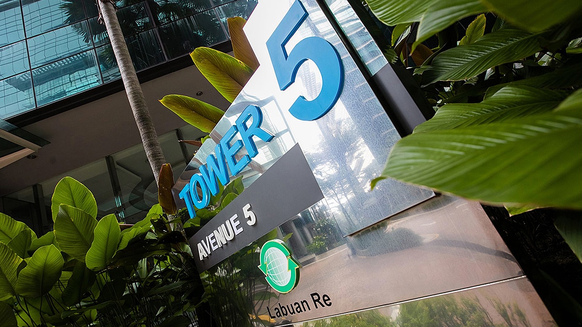 Building sign reading “Tower 5 Avenue 5 Labuan Re” surrounded by tropical plants.