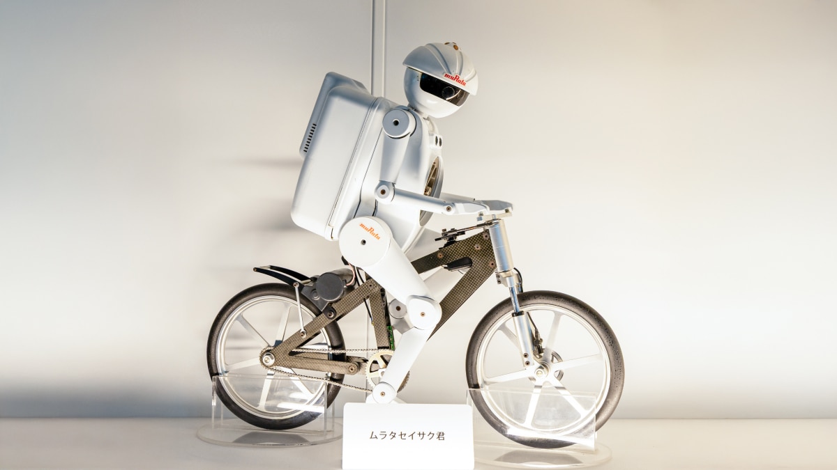 White humanoid robot labeled muRata riding a bicycle, displayed against light background.