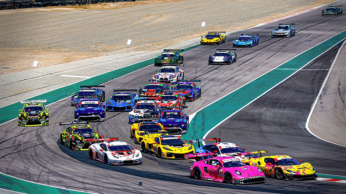 A colorful grid of IMSA GT race cars navigating a corner at Laguna Seca Raceway during a high-speed endurance competition.