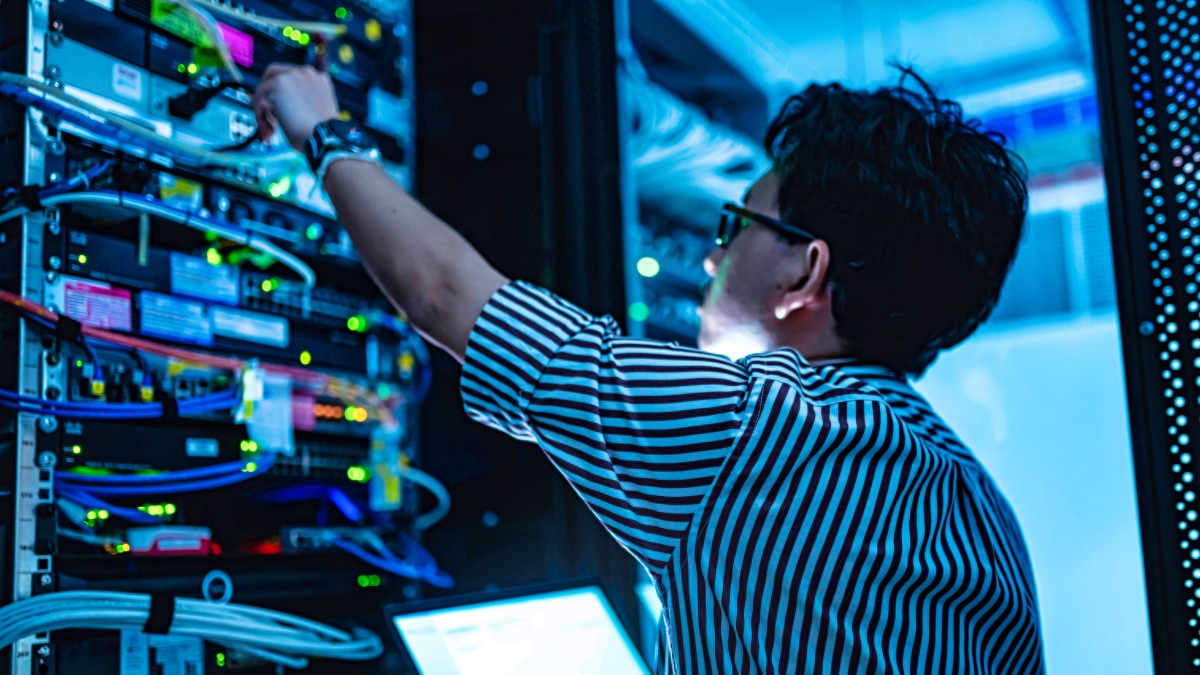Technician reaching into a lit server rack, adjusting network cables and hardware modules.