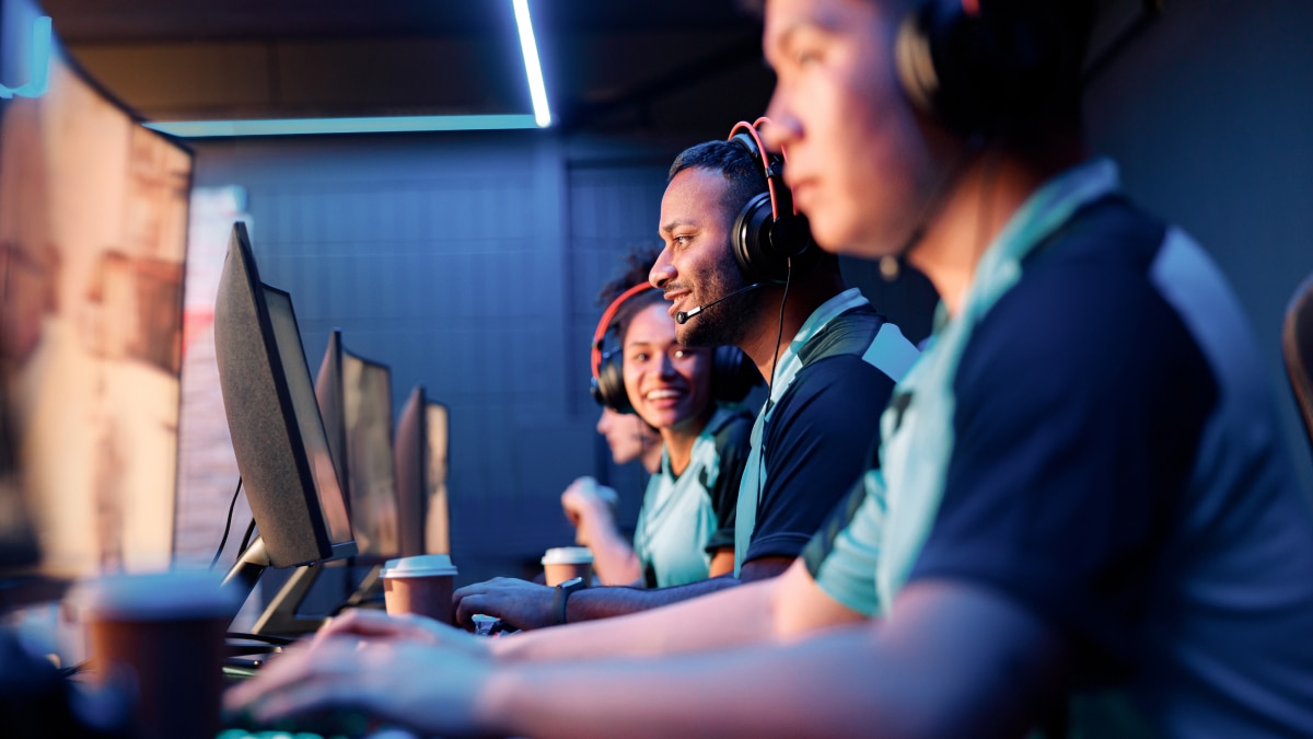 Esports players in headsets focused on monitors, smiling and communicating during gameplay.