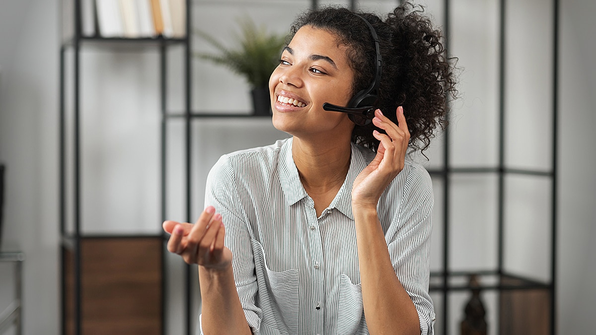 Two customer support agents wearing headsets work on laptops in a modern office with blue lighting.