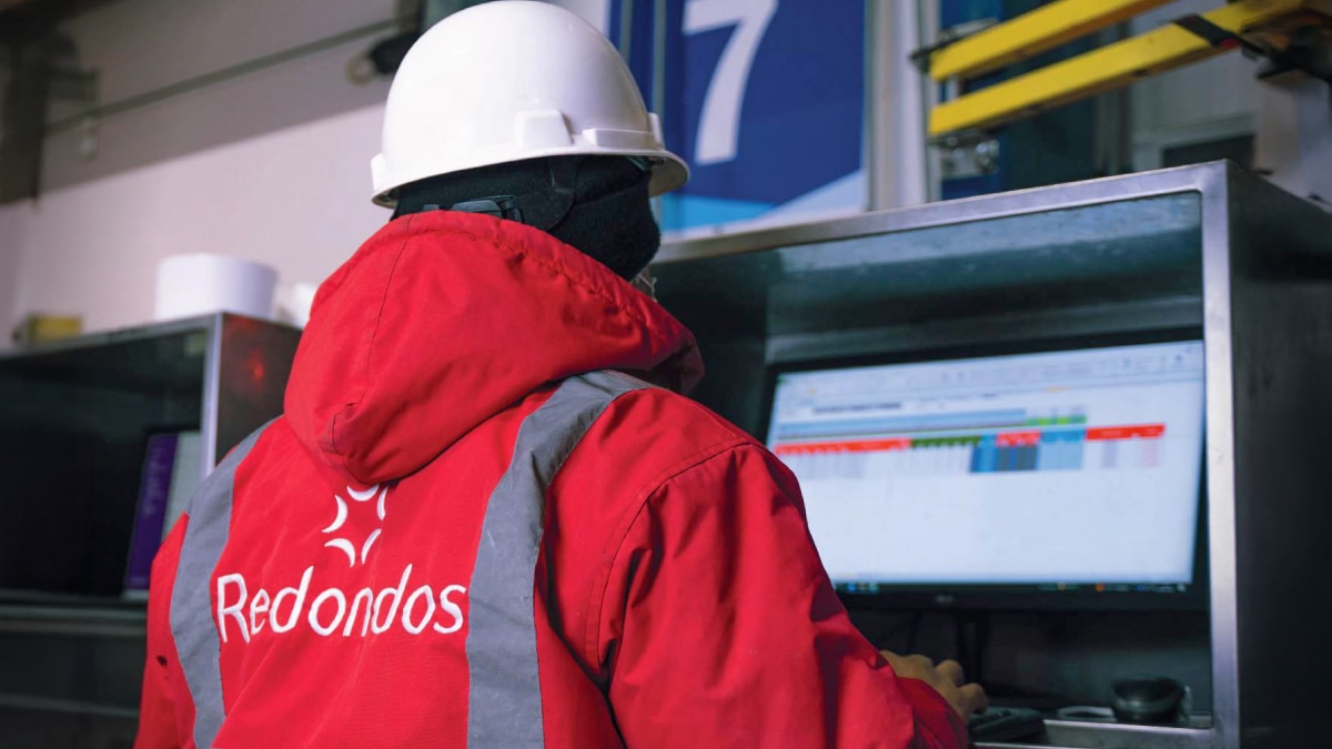 Redondos alimentos worker wearing a hard hat and red jacket monitors production data on a computer screen