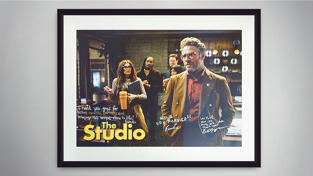 Framed poster reading “The Studio” with handwritten signatures; group of people in a warmly lit studio scene