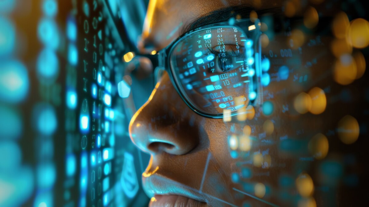 Close-up of face with glasses reflecting code and blue digital data patterns across the lens