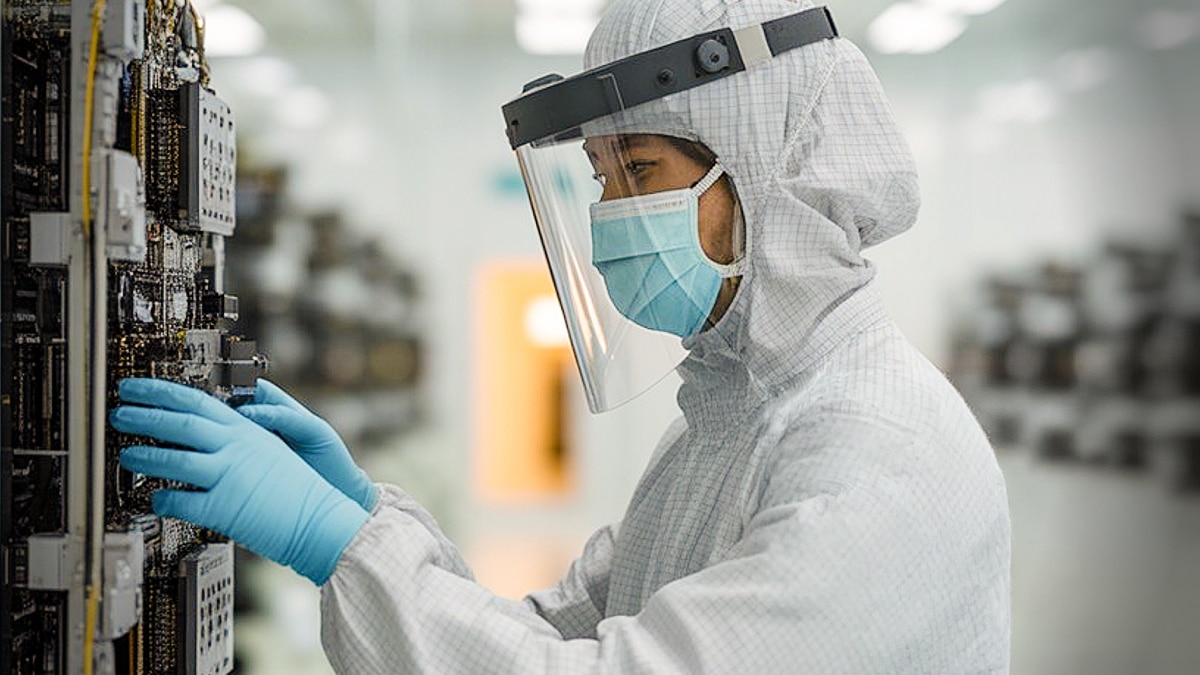 Technician in protective suit and face shield installs circuit board into equipment in sterile lab
