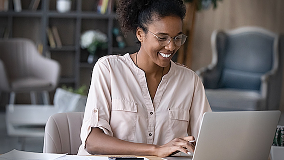 Woman smiling while working on a laptop in a home office environment.