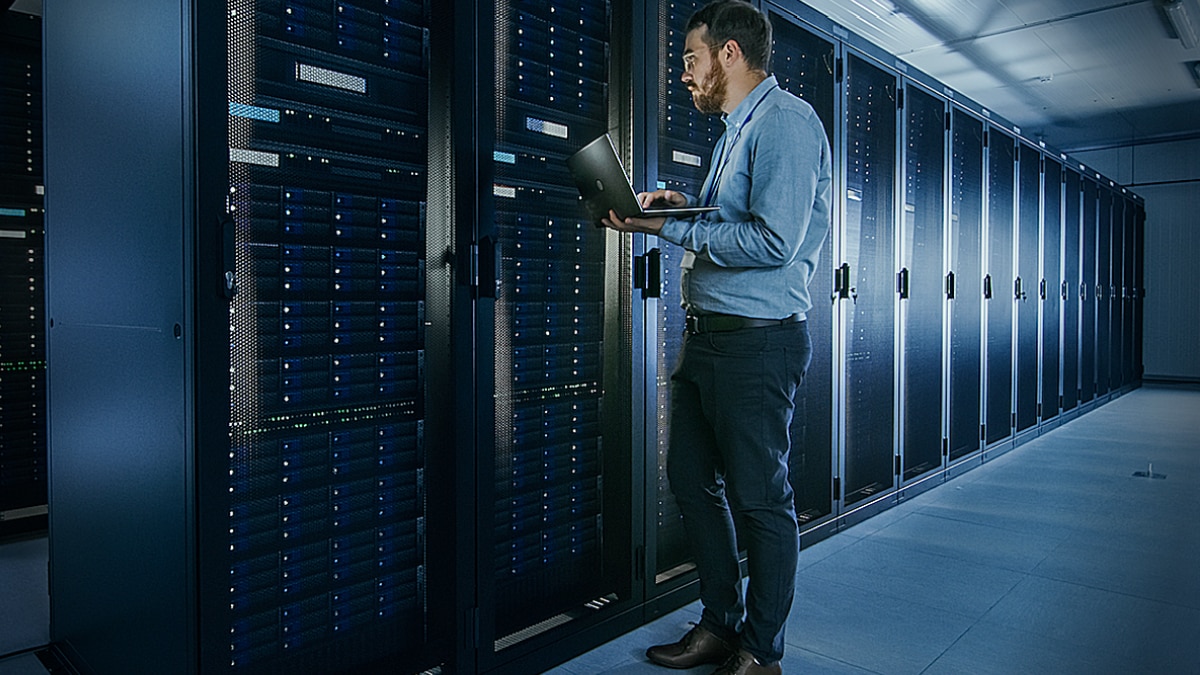 IT administrator using a laptop beside server racks in a data center.