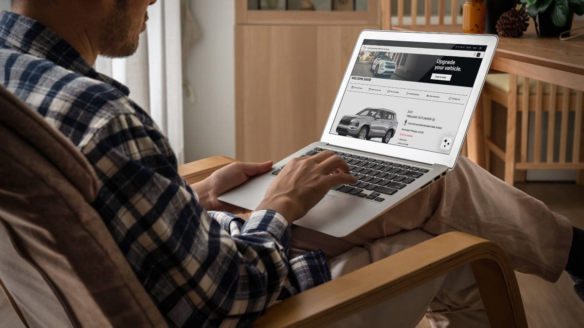 Person using a laptop at home to browse vehicle listings and upgrade options on a dealership website