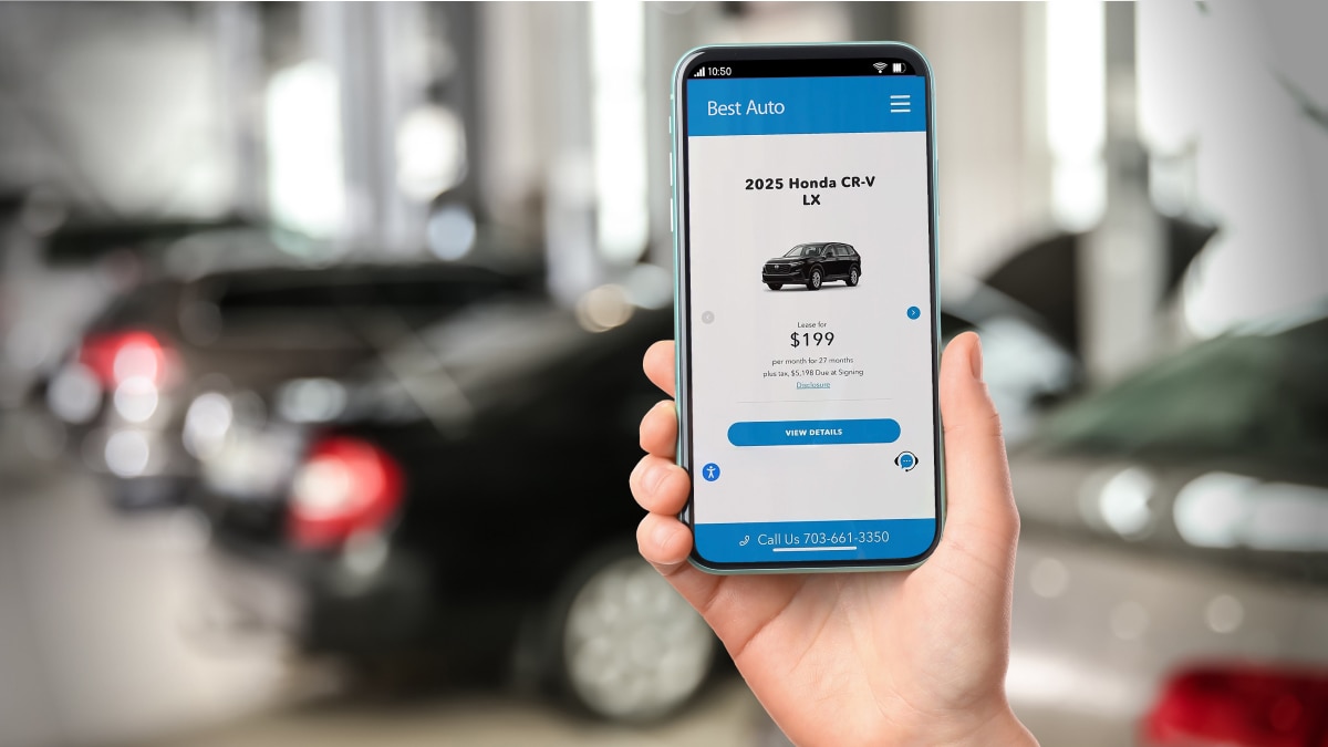 Hand holding smartphone displaying a vehicle lease offer app inside a blurred car dealership