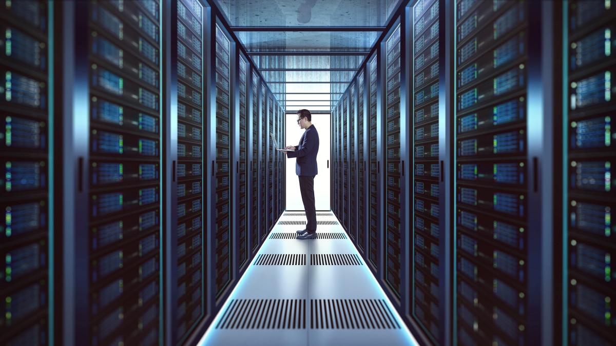 IT professional using a laptop in a server room between rows of illuminated data center racks