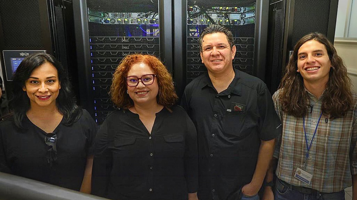 Four team members standing in front of Dell server racks inside a data center.