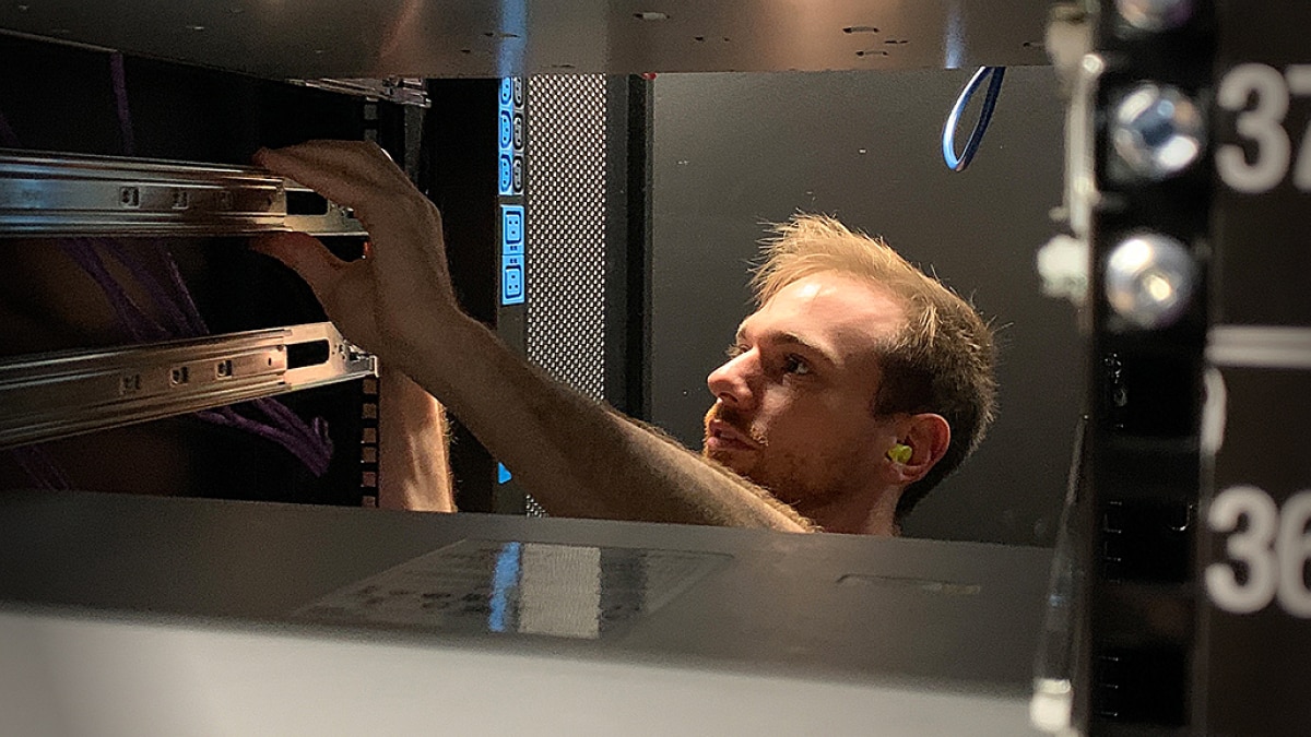 Technician installing server hardware in a data center rack with network cabling visible.