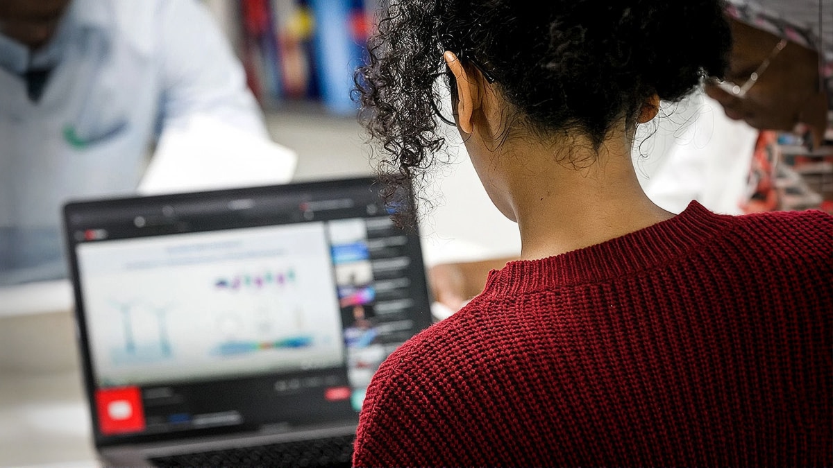 Student viewed from behind using a laptop displaying charts while studying with classmates in the background.