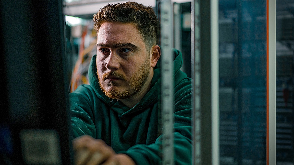 Technician works at a server rack in a data center, focused on equipment behind a glass cabinet door.
