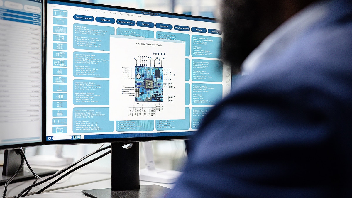 Computer monitor displays a blue circuit board diagram and technical design interface in a laboratory workspace.