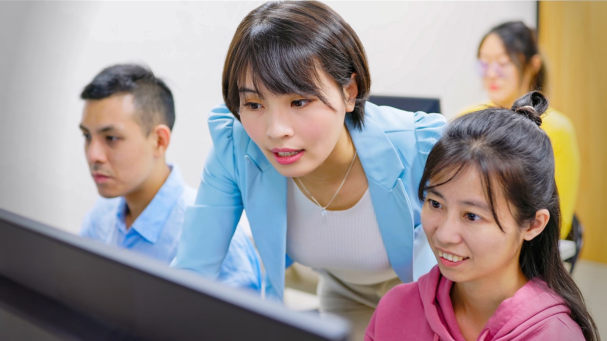 Three developers collaborate around a computer monitor in a bright workspace.