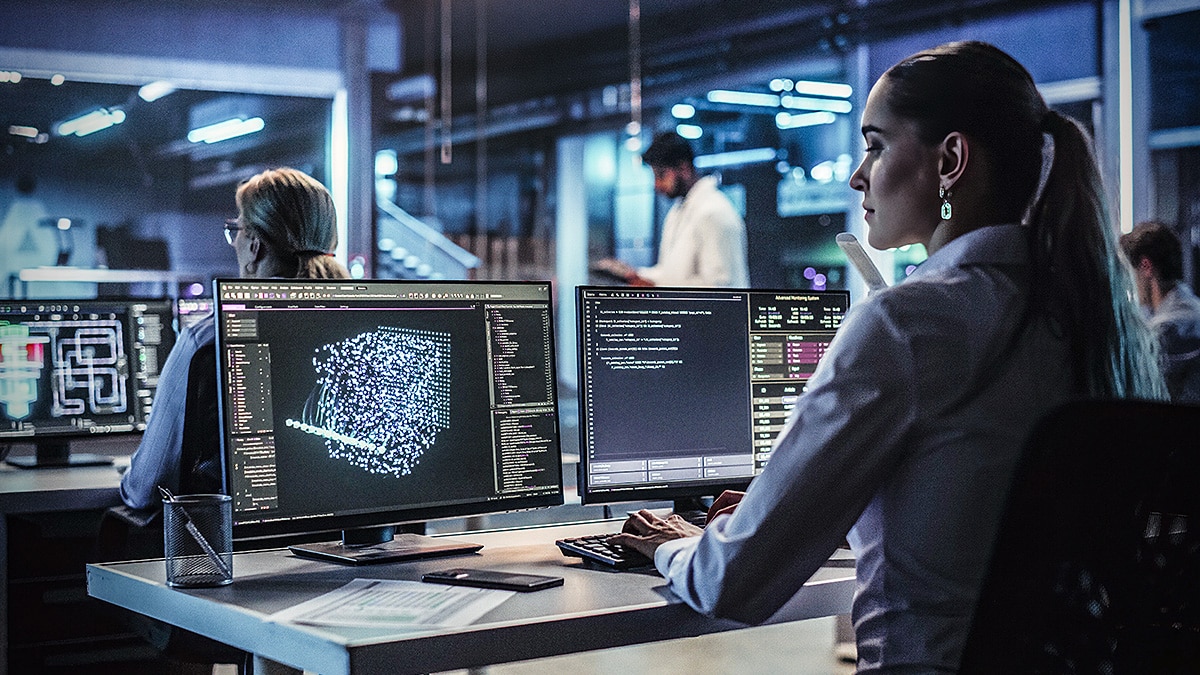 Developer works at dual monitors showing code and a blue 3D data visualization in a modern office.