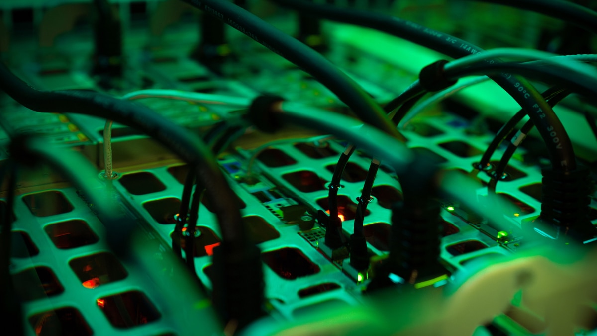 Close-up of server hardware under green lighting with connected black cables and illuminated status lights.